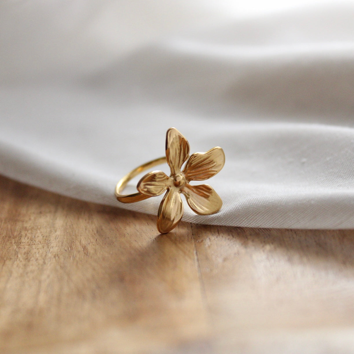 Bague dorée en forme de fleur en acier inoxydable posée sur tissu blanc