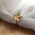 Bague dorée en forme de fleur en acier inoxydable posée sur tissu blanc