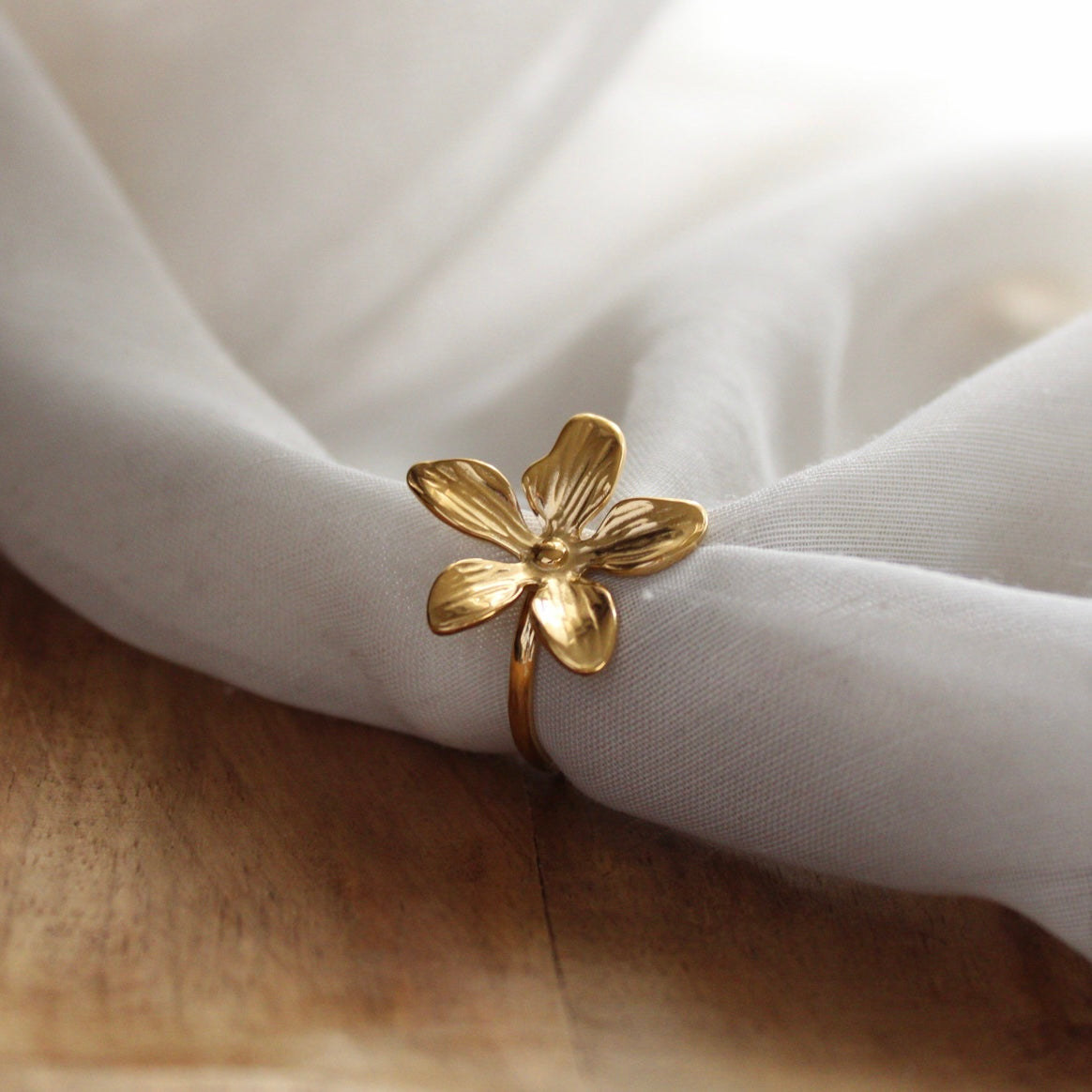Bague dorée en forme de fleur en acier inoxydable posée sur tissu blanc